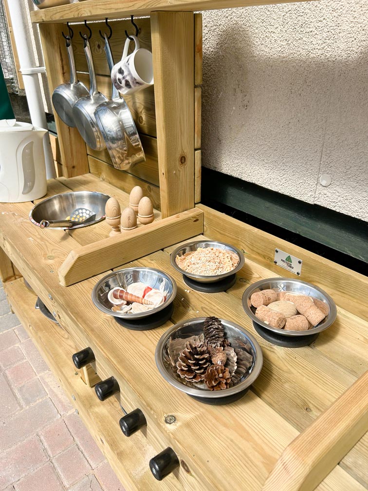 a wooden outdoor children's kitchen area with shells, pinecones and corks set up