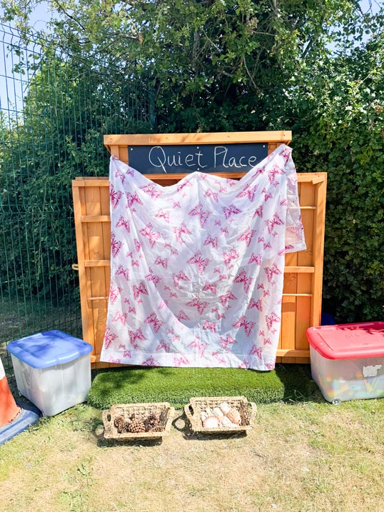 a shed with a curtain over it and a sign that says 'quiet place' outside on a sunny day with toys in the grass in front