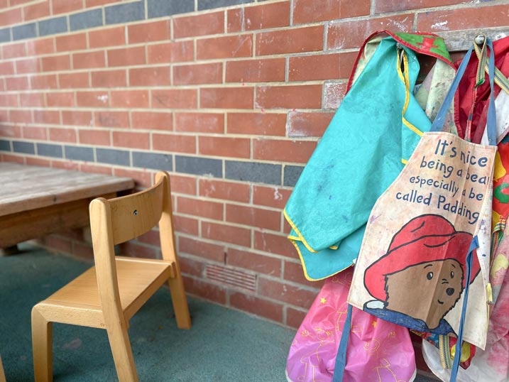 a brick wall with children's aprons hanging up and a child's chair and table