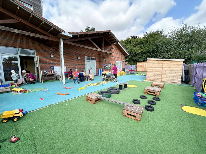 An outdoor play area for children outside a nursery with toys and play sets and children playing in the background