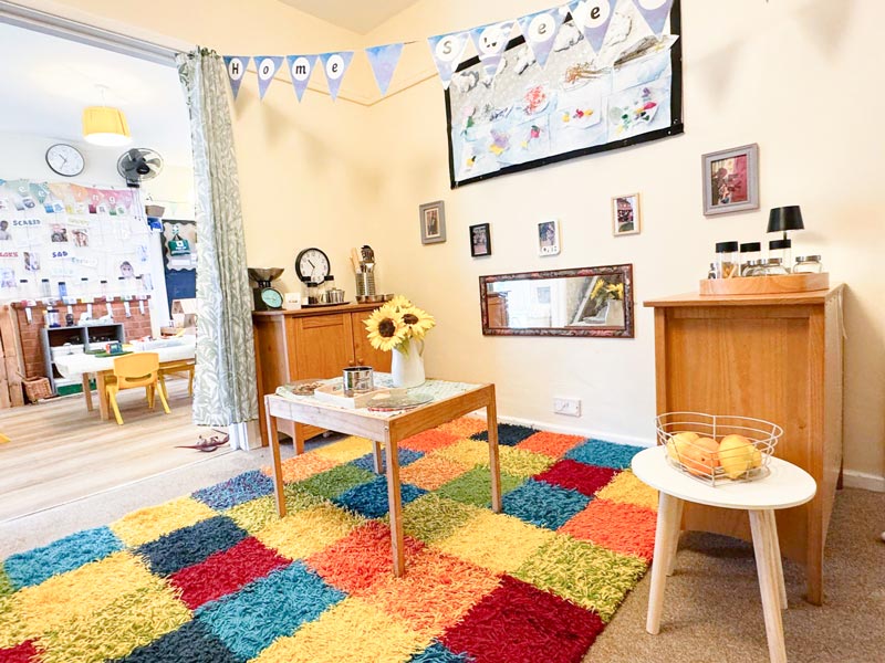 a children's nursery room with cabinets, a colourful rug, activities, and flowers