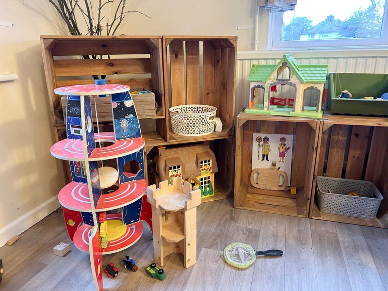 a corner in a nursery room with children's toys including doll houses and a space ship