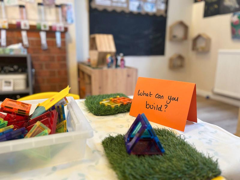 a table in a nursery room with building toys and a sign that says 'what can you build?'