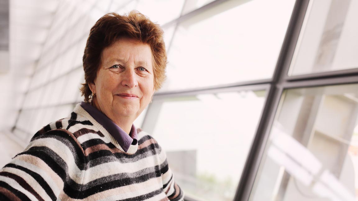 a woman with short brown hair stands in front of a window and smiles at the camera