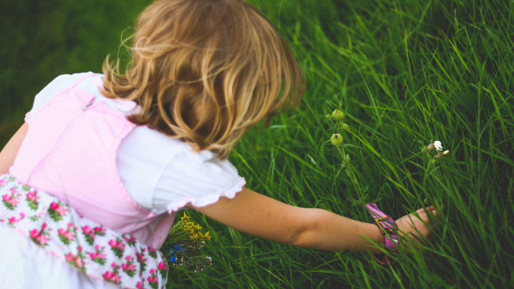 a young girl with blonde hair reaching for a flower